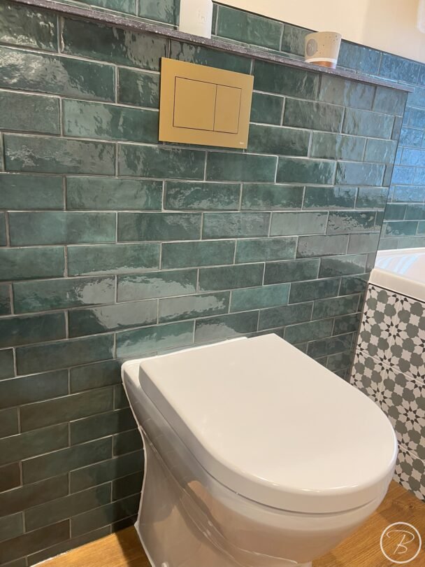 close up of wc on green metro tiles with brushed bronze flush plate